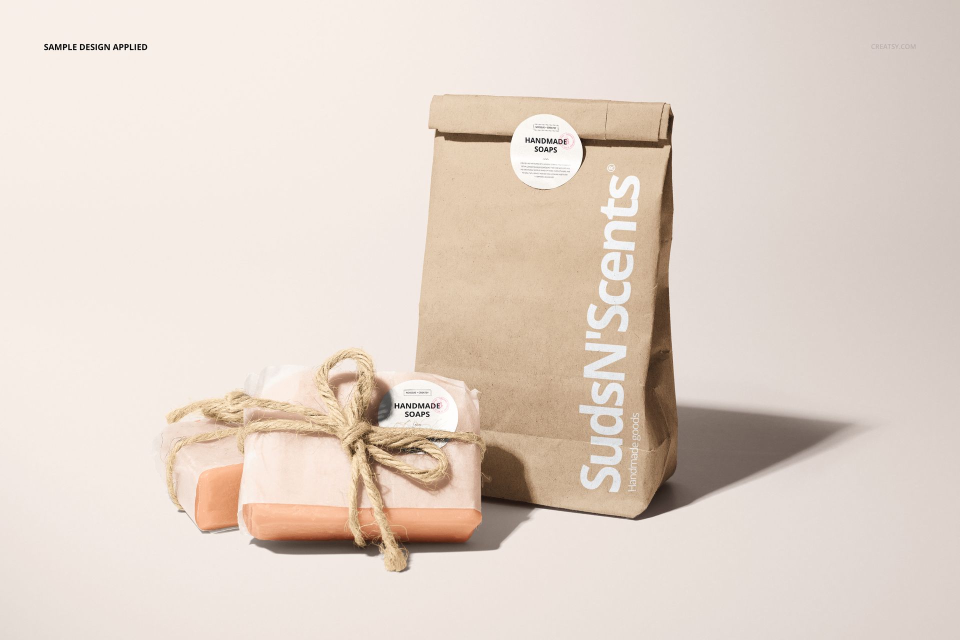 Handmade soap packaging mockup featuring a brown paper bag and two wrapped soap bars tied with twine on a light surface.