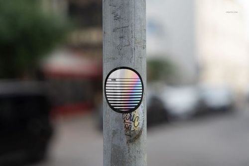 PSD mockup showing a circular sticker with striped design and rainbow colors placed on a vertical metal pole.