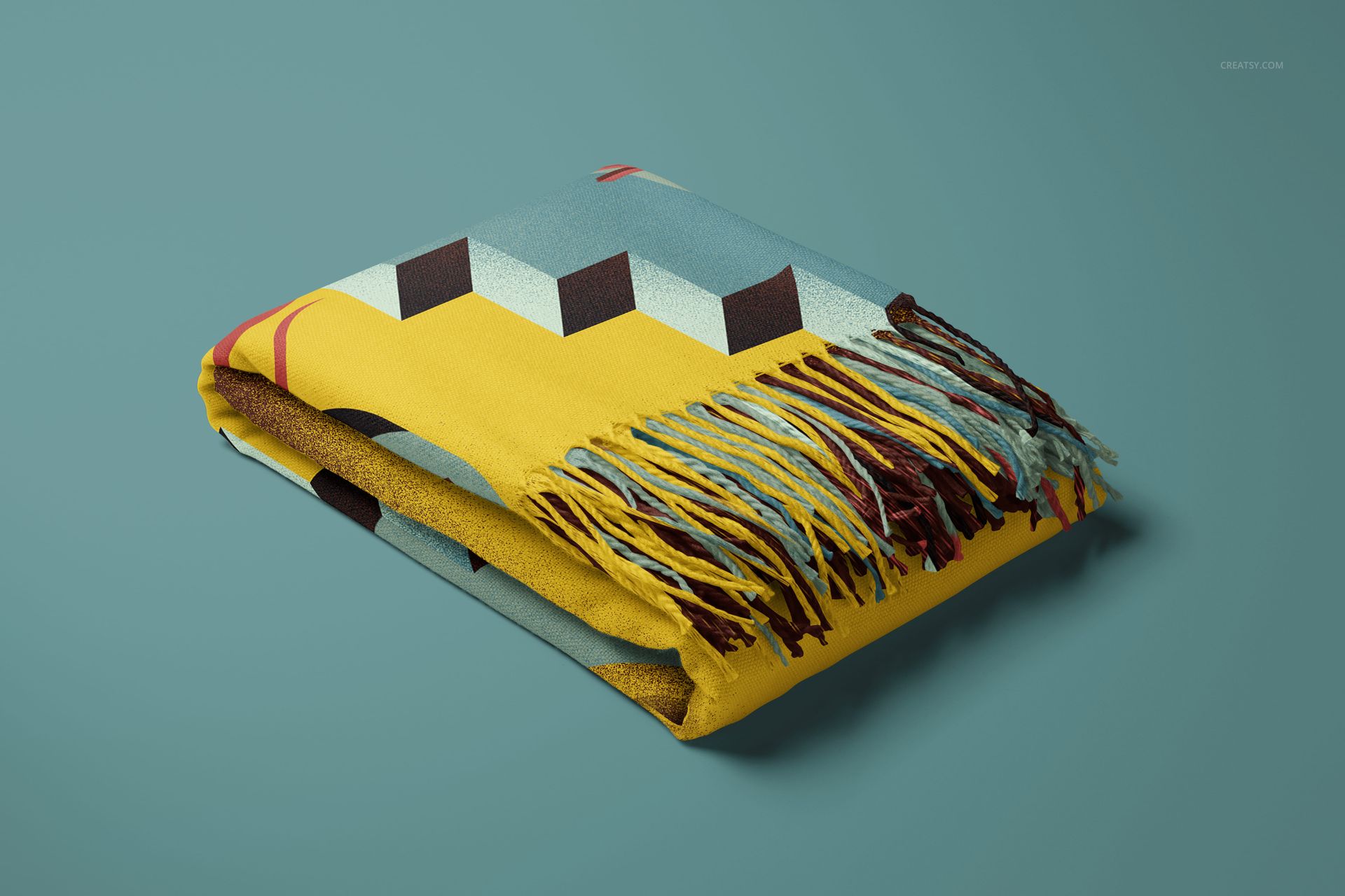 Tassel fringe blanket mockup showing folded fabric with bold geometric design in yellow, blue, and brown tones.