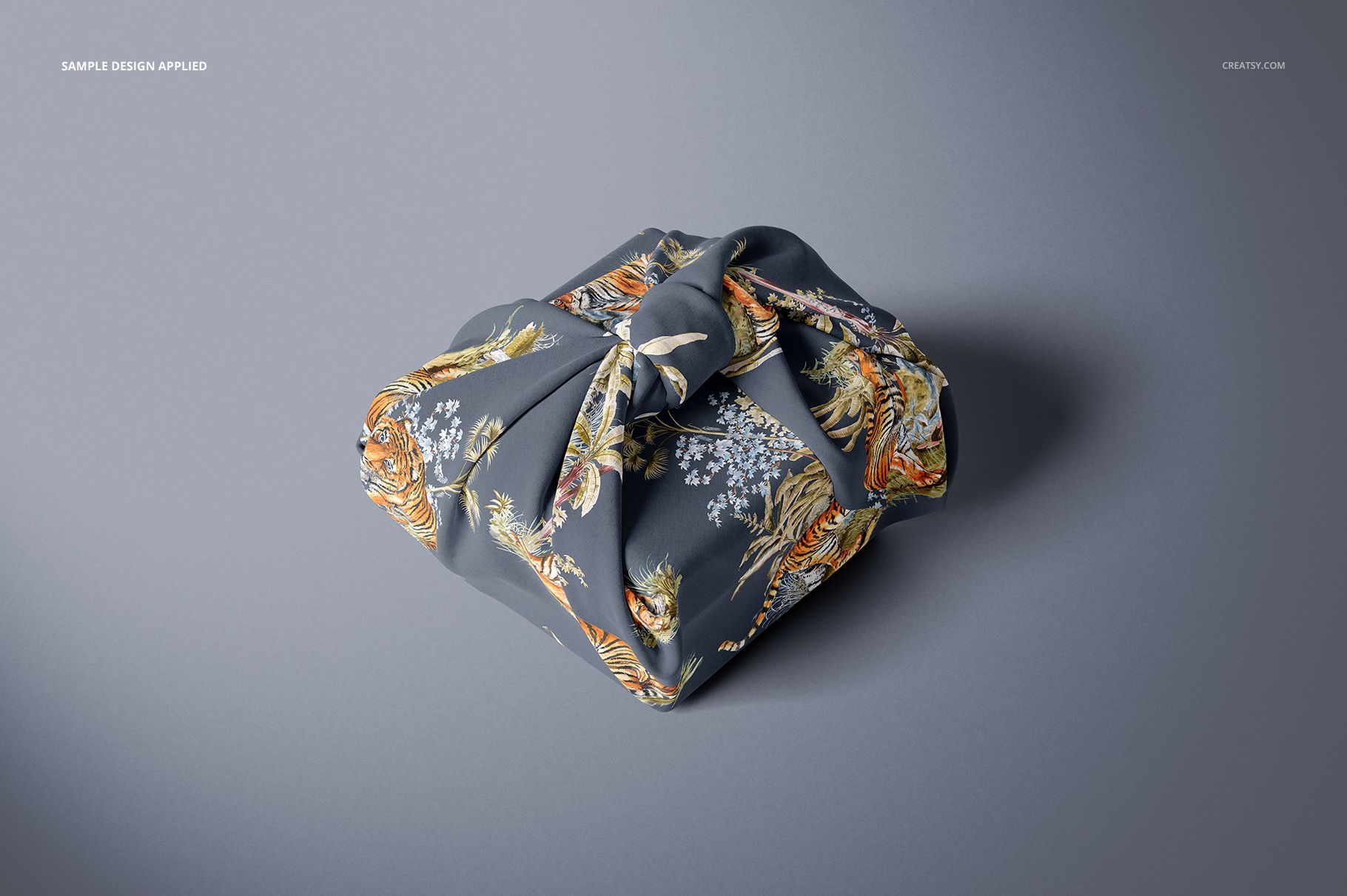 Fabric gift wrap mockup featuring a square package wrapped in dark fabric with floral and tiger patterns, top view.