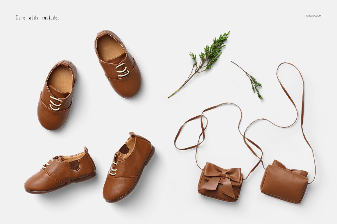 Brown baby shoes and two small brown purses with a bow, displayed on a white surface with green sprigs.