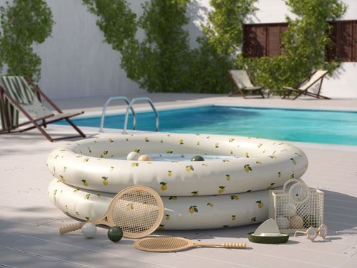 Round inflatable children's pool mockup in white with yellow fruit print, placed on a patio beside a pool and surrounded by play items.