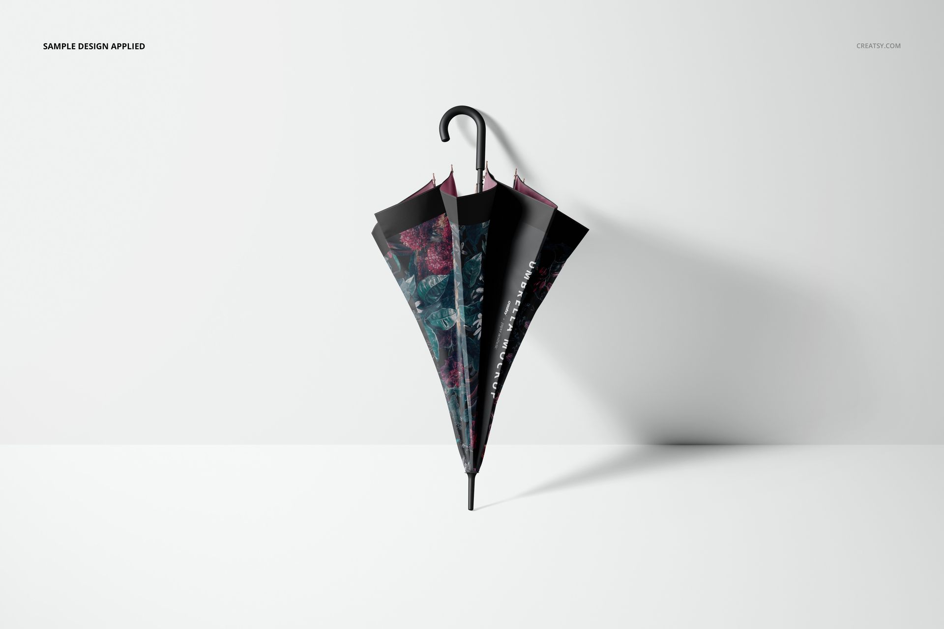 Closed umbrella with a dark floral pattern leaning against a white wall, shown in a fashion accessories mockup scene.
