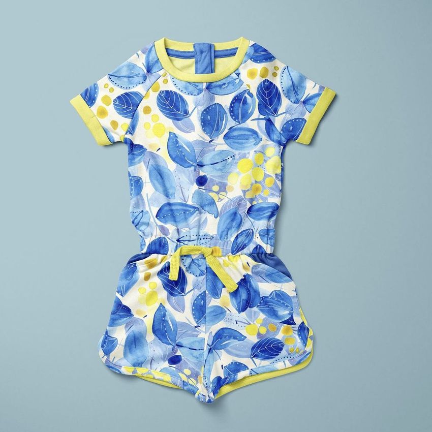 Girls cotton playsuit mockup featuring a short-sleeve one-piece with a blue and yellow floral pattern on a light blue background.