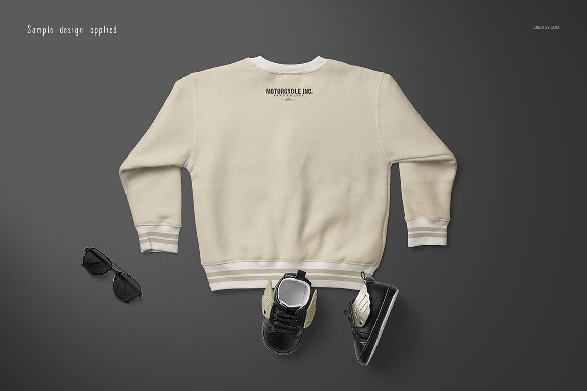 Beige baby sweatshirt mockup displayed from the back on a dark surface, with shoes and sunglasses beside it.