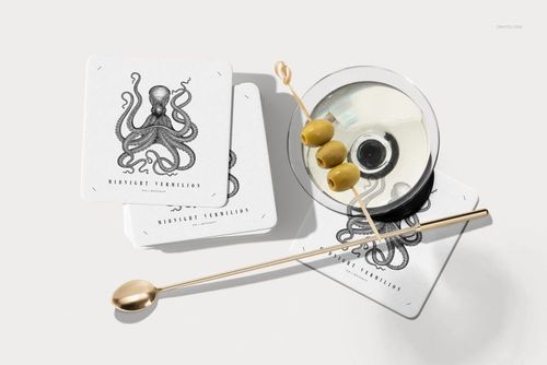 PSD mockup of square coasters with monochrome octopus artwork, shown beside a martini and cocktail accessories.