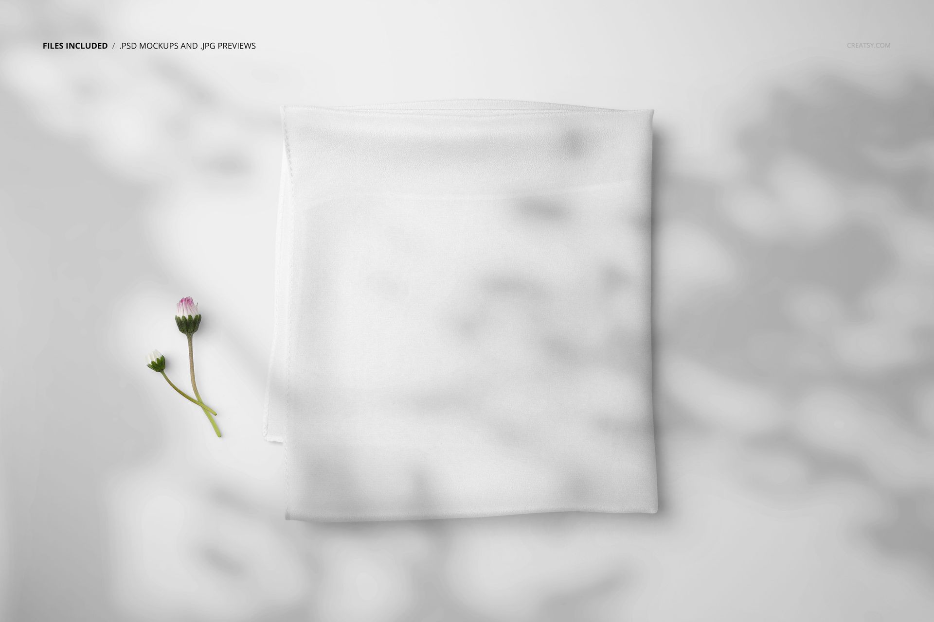 White silk scarf mockup shown folded neatly, viewed from above, next to a delicate flower and shadow patterns.