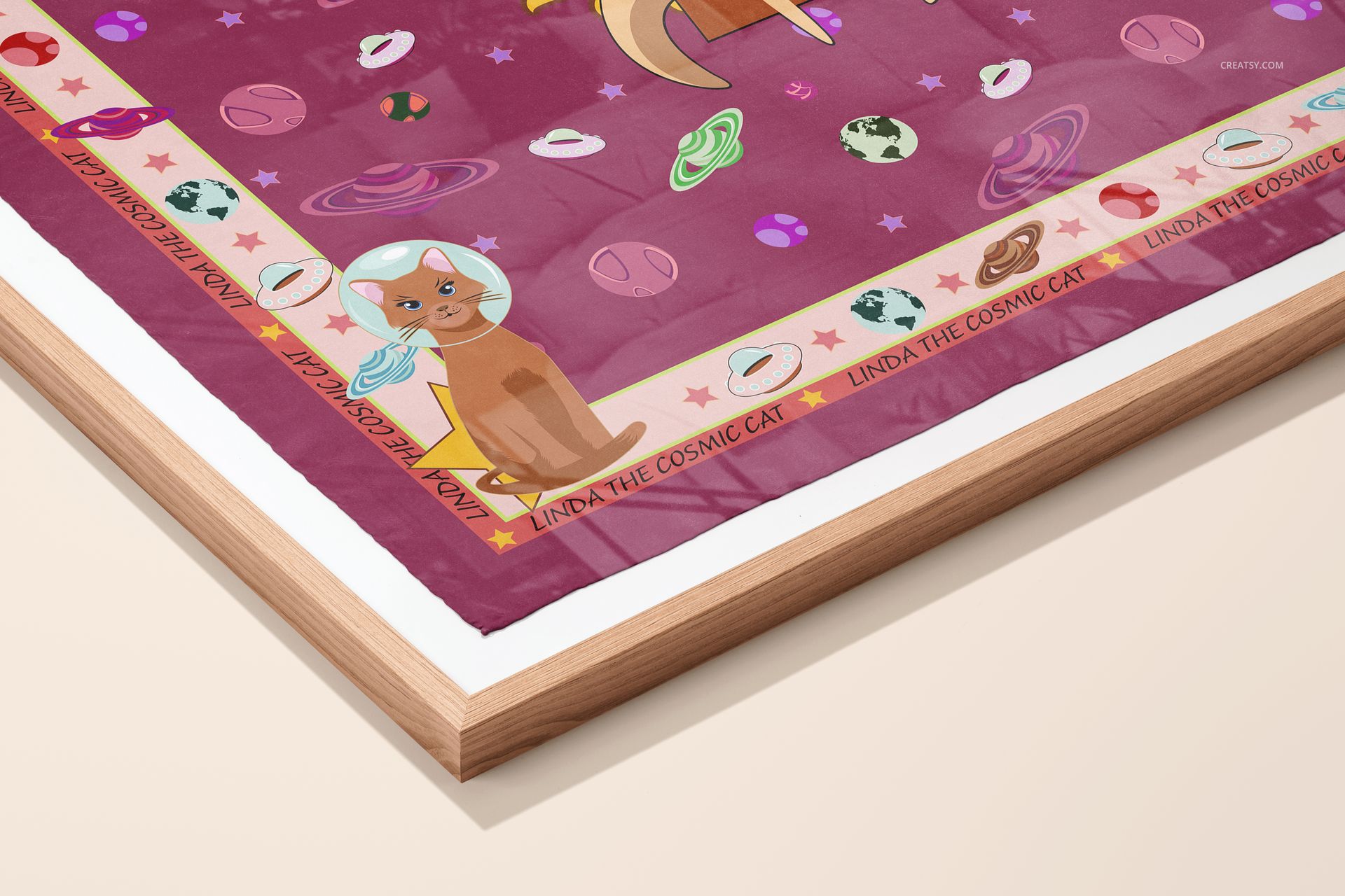Corner view of a framed silk scarf featuring cartoon cats, planets, and stars on a magenta background, presented as a mockup.
