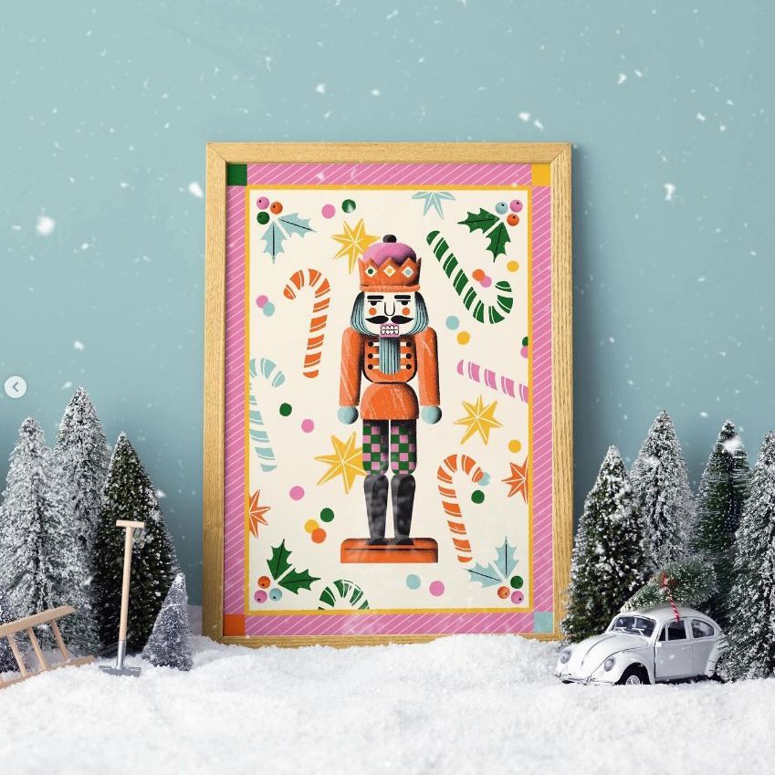Christmas picture frame mockup featuring a nutcracker illustration, surrounded by candy canes and festive patterns, set in snow with miniature trees and a white toy car.