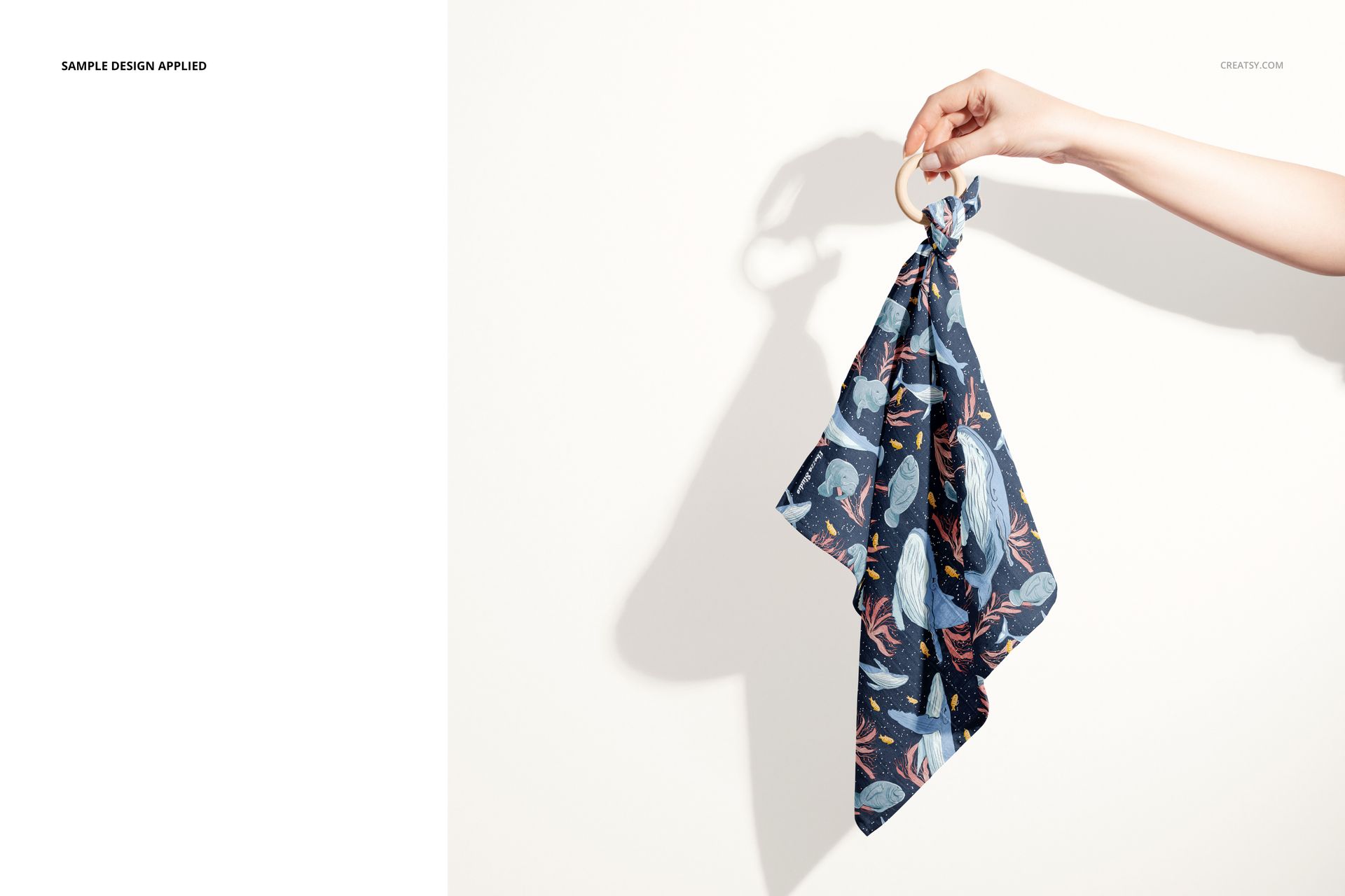 Muslin cloth wooden teether mockup featuring a hand holding a ring with dark blue fabric and animal designs.