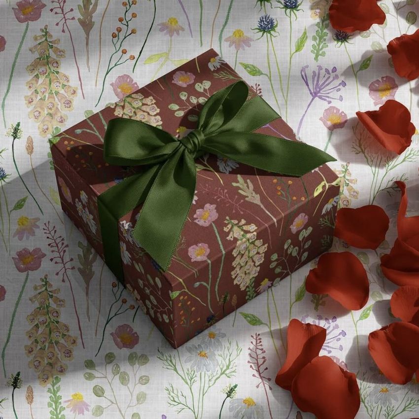 Square gift box mockup with a dark floral pattern and green ribbon, surrounded by scattered red rose petals on a floral surface.