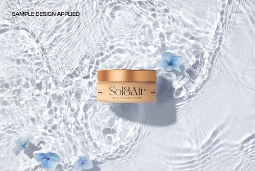 Frosted glass cosmetic jar with gold lid resting in clear water with ripples and blue flowers, top view mockup.