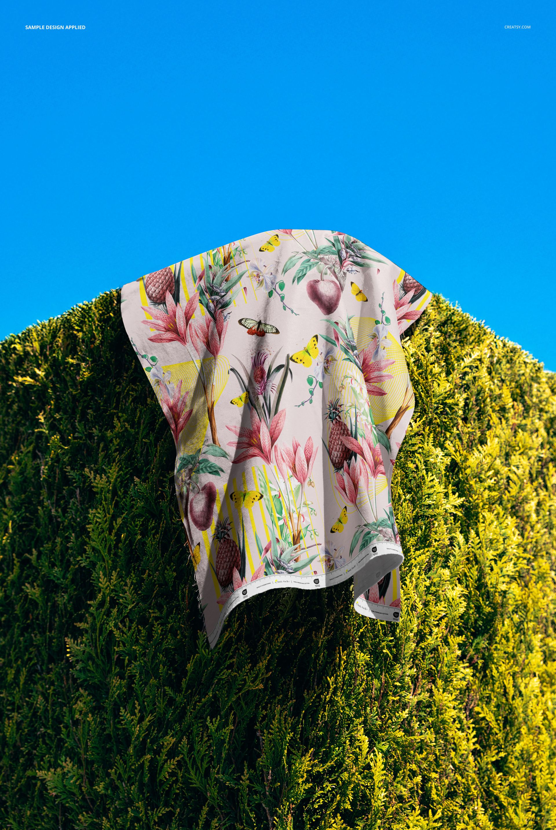 PSD mockup showing cotton fabric featuring a vibrant floral and bird design hanging on a lush green hedge.