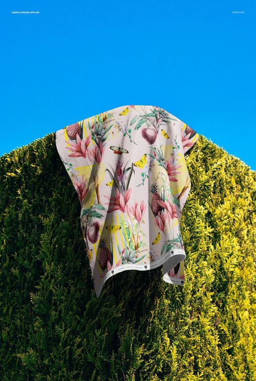 PSD mockup showing cotton fabric featuring a vibrant floral and bird design hanging on a lush green hedge.