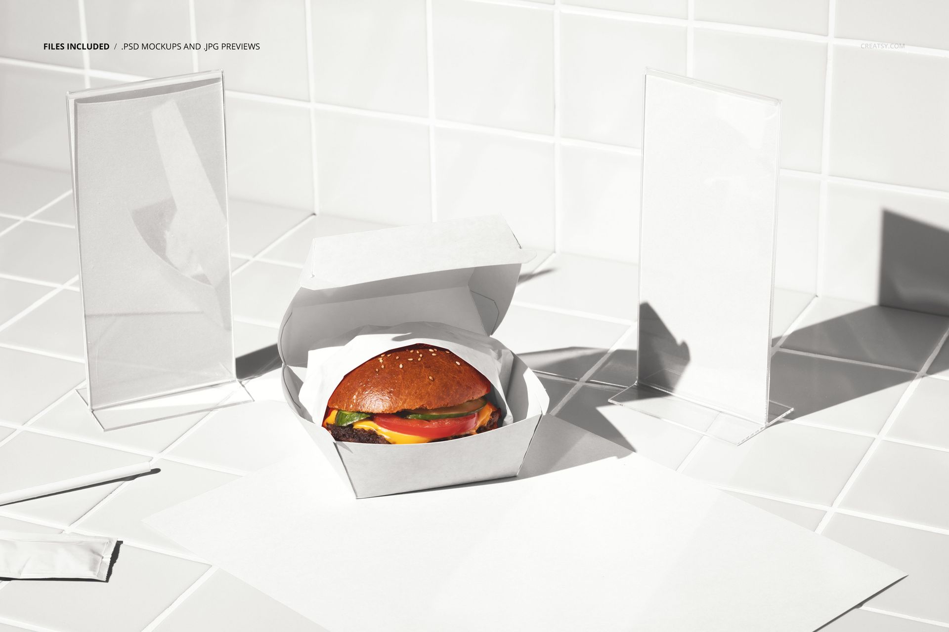 PSD mockup featuring a burger in packaging with empty menu stands and white paper elements on a tiled countertop.