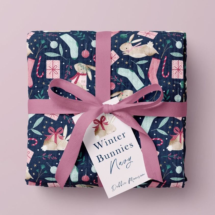 Crinkle muslin swaddle blanket mockup featuring a folded blanket with a winter bunny pattern, tied with a pink ribbon on a pastel background.