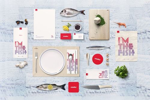 Seafood restaurant table setting mockup with plates, cutlery, fish, menu cards, and fresh ingredients on a light wood surface.