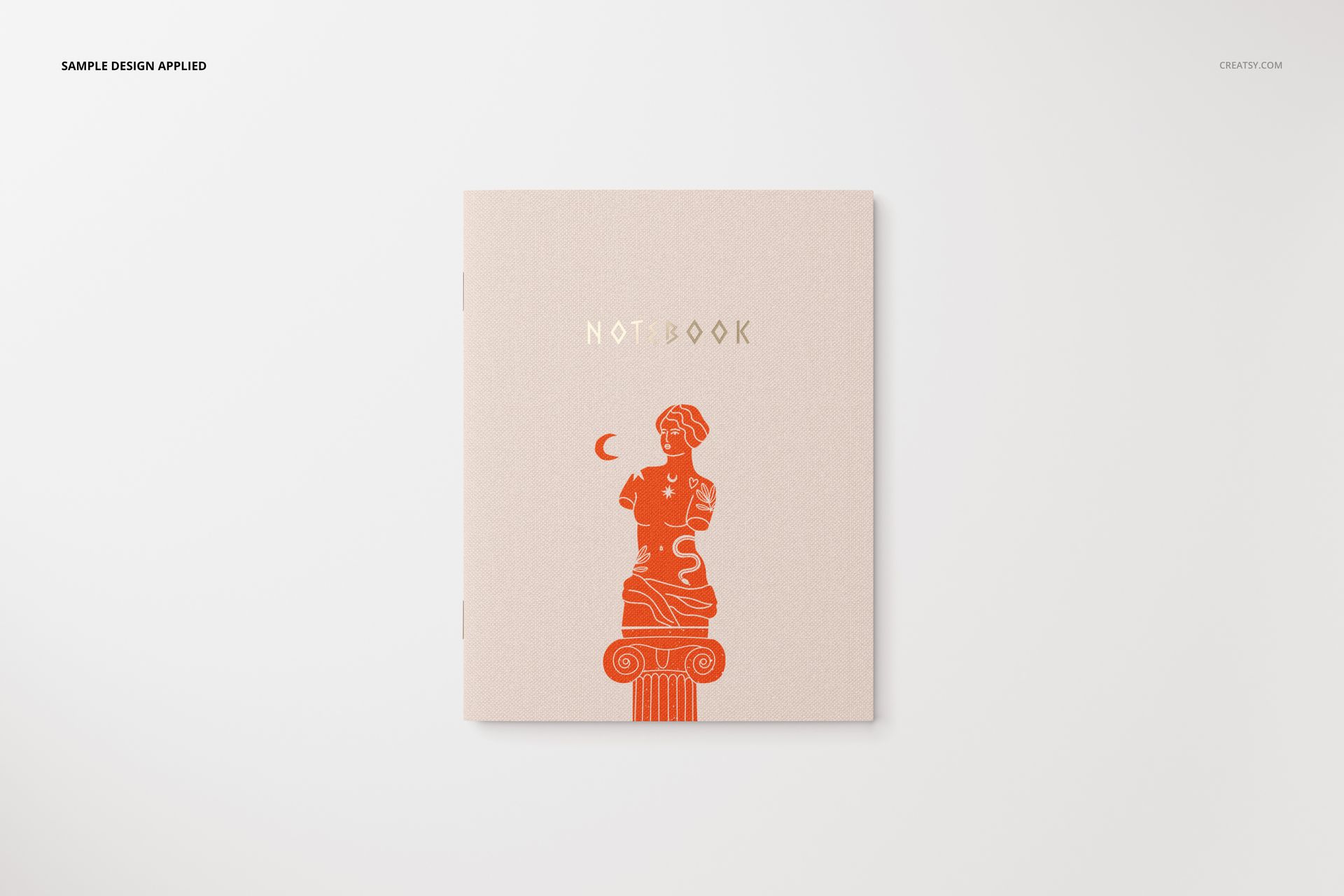 Stationery mockup showing a closed notebook with minimalist artwork and gold lettering, viewed from above on a plain background.