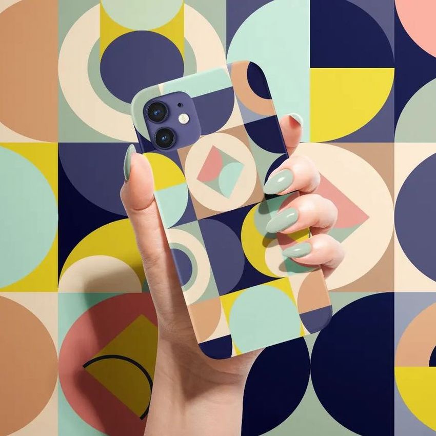Hand holding an iPhone 12 matte snap case with a bold geometric pattern in blue, yellow, and pastel colors, matching the abstract background.