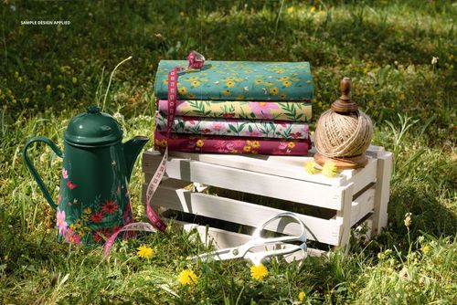 PSD mockup showing patterned fabric bundles on a crate in a sunlit meadow, surrounded by garden props and wildflowers.