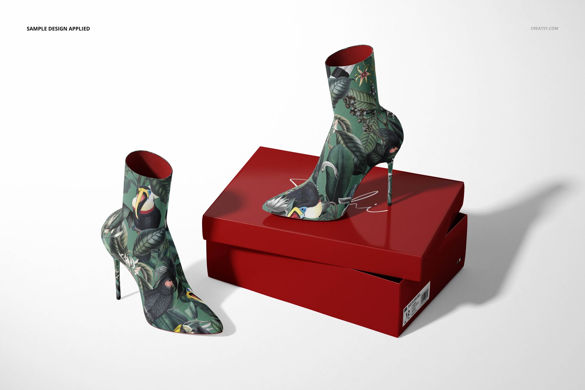 Front angle of mockup showing fabric ankle boots with a botanical print, positioned next to a closed red shoebox.