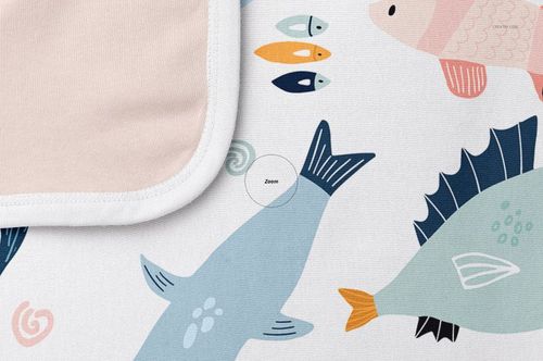 Cotton baby blanket mockup featuring a close-up of playful fish illustrations and a folded corner with a soft pink lining.