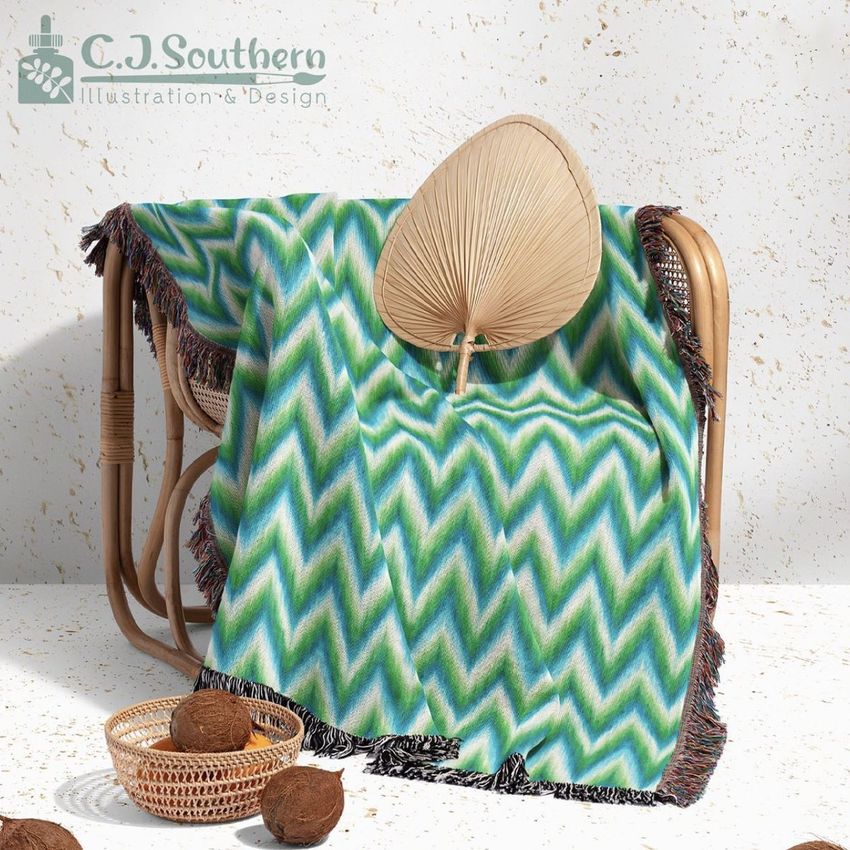 Woven throw blanket mockup draped over a rattan chair, featuring a green and blue zigzag pattern and fringed edges.