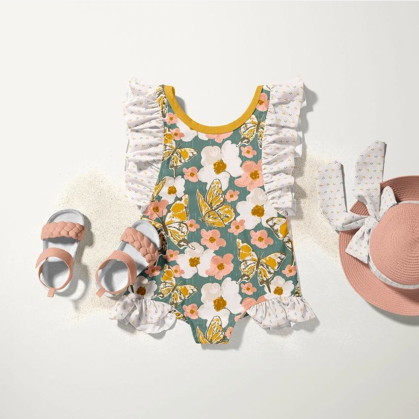 Baby ruffle swimsuit mockup featuring a floral and butterfly pattern, styled with pink sandals and a matching sun hat on a light background.