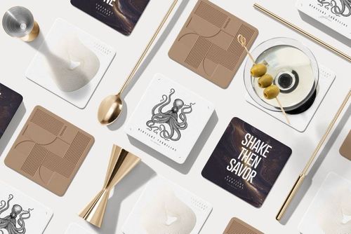 Top view of square coasters mockup set featuring abstract and text patterns, surrounded by barware and olives.