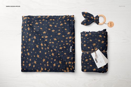 Muslin swaddle blanket mockup set featuring a dark fabric with yellow star pattern, shown folded and rolled with wooden teether on a light surface.