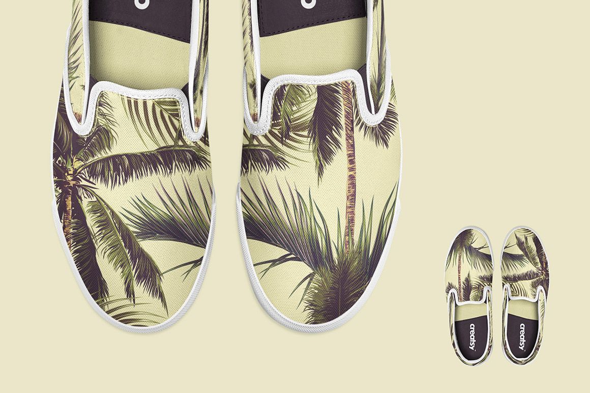 PSD mockup of slip-on shoes with a leafy palm design, arranged with two pairs on a pale beige surface.