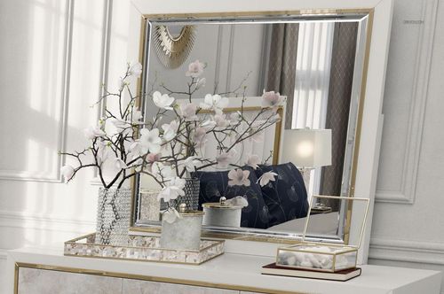 Front view of a luxury bedroom scene with a decorative mirror, white dresser, and flower arrangement in the foreground.