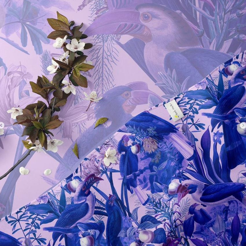 Closeup of a machine hemmed silk scarf mockup with a purple jungle bird pattern, displayed on a matching botanical background.