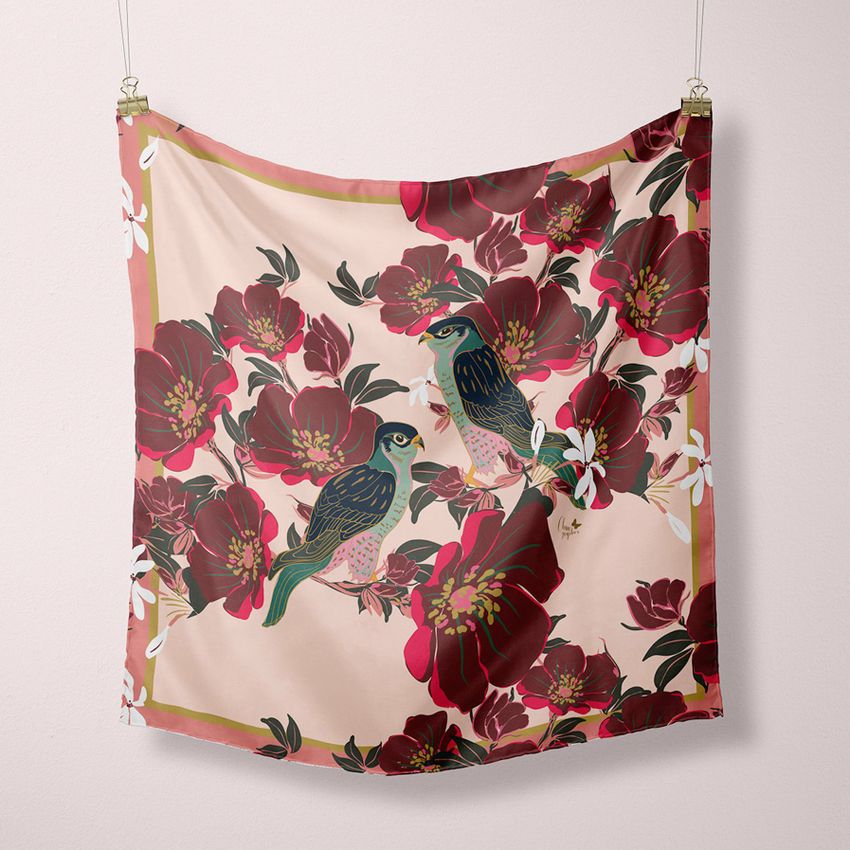 Hanging square silk scarf mockup featuring a floral pattern with large red flowers and two illustrated birds on a pale background.