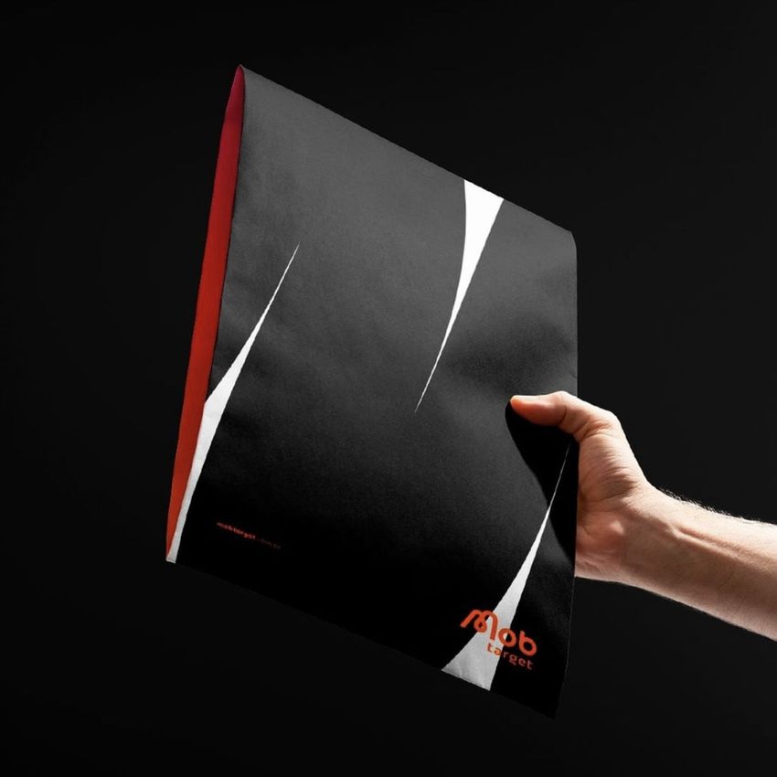 Hand holding a kraft mailer mockup with a black front, bold white diagonal accents, and orange interior against a dark background.