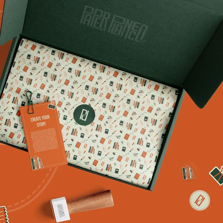 Mailing box mockup with an open dark green lid, patterned tissue paper inside, and a branded card on an orange surface.