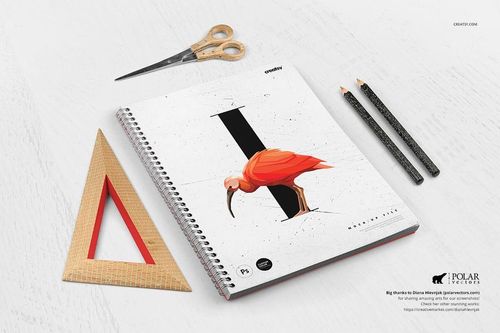 Front view of a mockup notebook with a graphic bird on the cover, placed beside drawing tools and a triangular ruler.