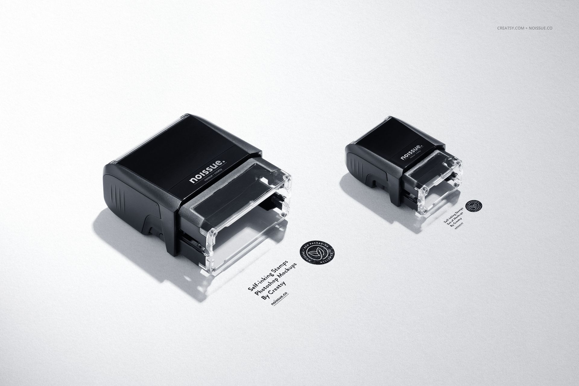 Two self-inking stamps in black casing shown on a light surface, each leaving a circular black ink imprint nearby.