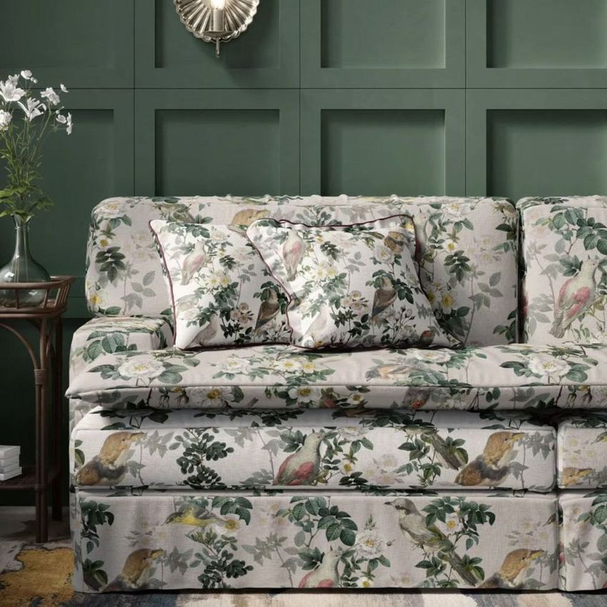 Upholstered sofa mockup in a living room, featuring floral and bird patterned fabric, green paneled wall, and decorative accents.