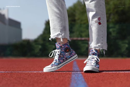 PSD mockup featuring floral high-top sneakers on a red running track, person standing with green trees in the background.