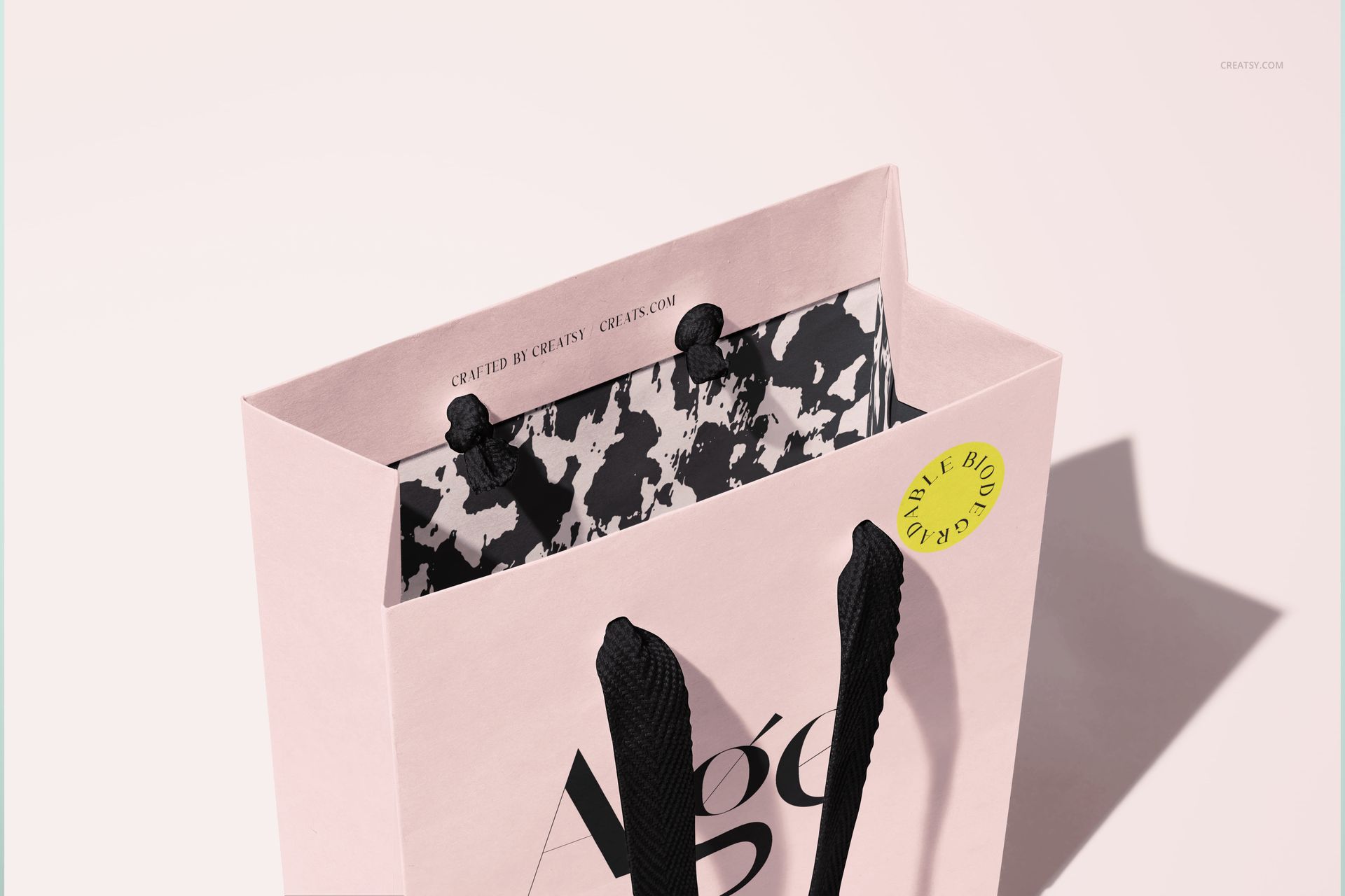Elegant paper gift bag mockup in soft pink, displaying black handles and patterned interior under bright lighting.