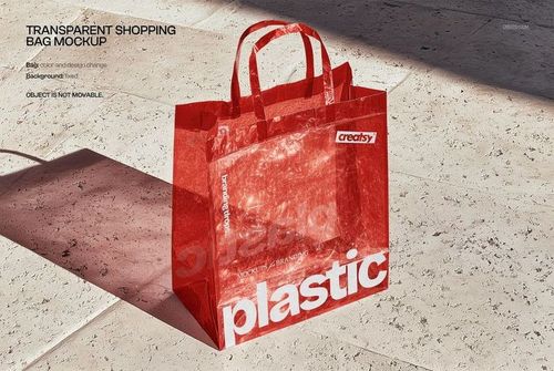 Red transparent plastic shopping bag mockup with handles, placed on a light stone floor in natural sunlight.