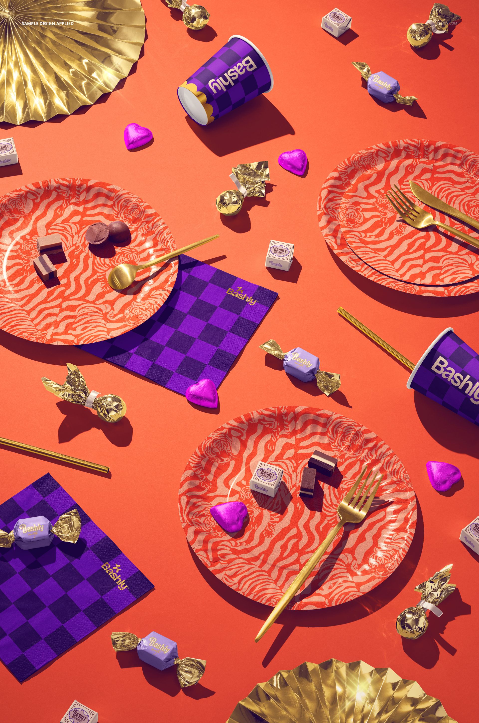 Disposable party tableware mockup featuring patterned plates, gold utensils, and cups on an orange surface.