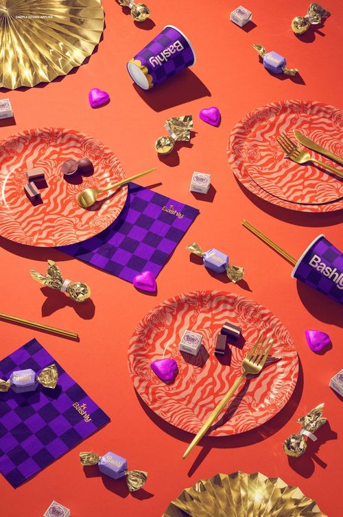 Disposable party tableware mockup featuring patterned plates, gold utensils, and cups on an orange surface.