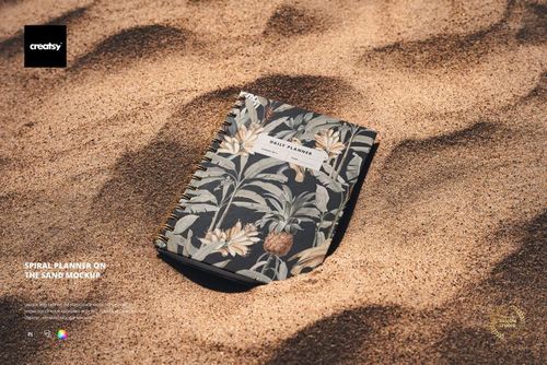 Top view of a spiral-bound planner featuring floral patterns, placed on sandy ground for a stationery mockup.