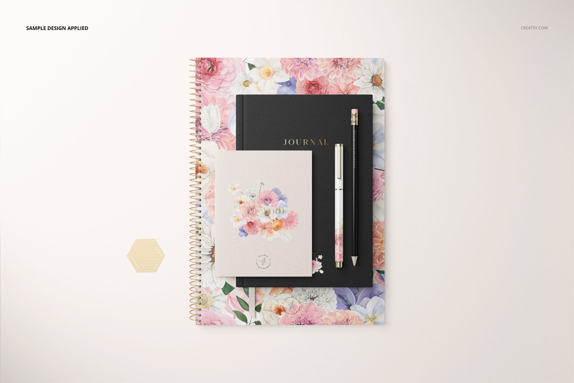 Stationery set mockup featuring a spiral notebook with colorful floral cover, black journal, card, pencil, and pen arranged neatly.