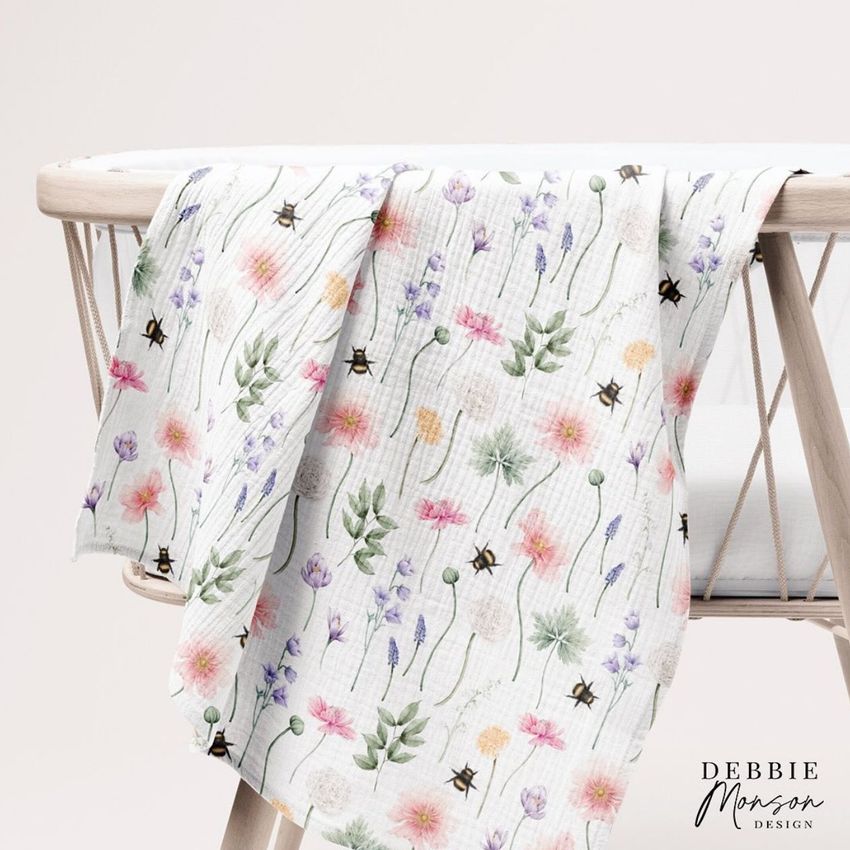 Crinkle muslin swaddle blanket mockup draped over a light wooden crib, featuring a delicate floral pattern on white fabric.