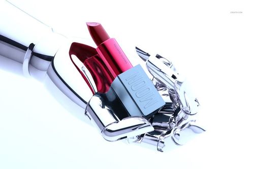 Lipstick mockup featuring a silver robotic hand with a red lipstick and blue rectangular case, illuminated by soft lighting.
