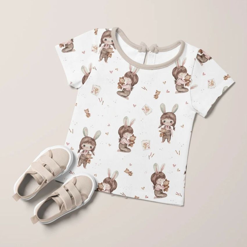 Kids t-shirt mockup with a cute bunny girl pattern, paired with beige sneakers on a light neutral background.