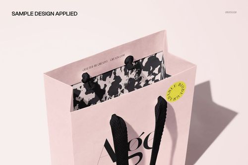 Close-up of a paper shopping bag mockup with light pink exterior, black braided handles, and patterned inner lining.